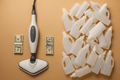 "A stylized flat lay image showing a single, modern steam mop with a small, neat pile of US Dollar bills ($100 or more) next to it, sharply contrasted with a large, messy stack of empty, discarded plastic cleaning chemical bottles. Visual theme: sustainability and cost savings."