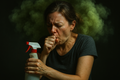 "Concept Art: A stressed woman is visibly coughing while holding a traditional cleaning spray bottle. A dense, toxic-looking cloud of green fumes surrounds her head, symbolizing lung irritation and indoor air pollution. High contrast, dramatic lighting, realistic photo style."